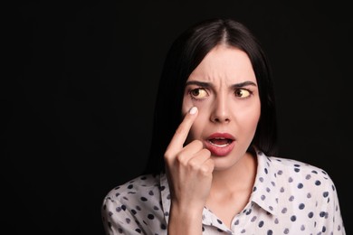 Woman checking her health condition on black background, space for text. Yellow eyes as symptom of problems with liver