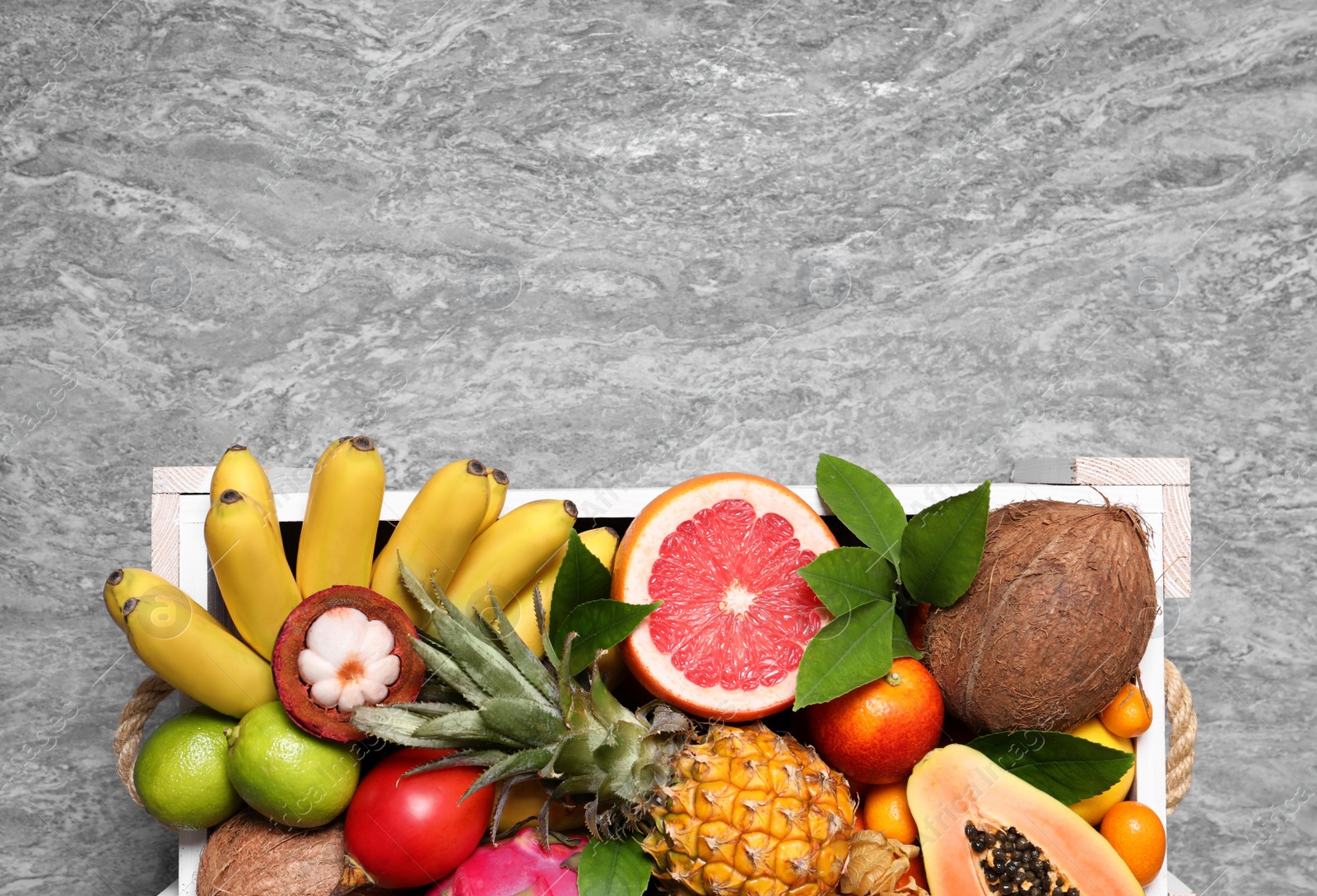 Photo of Different tropical fruits in wooden box on grey background, top view. Space for text