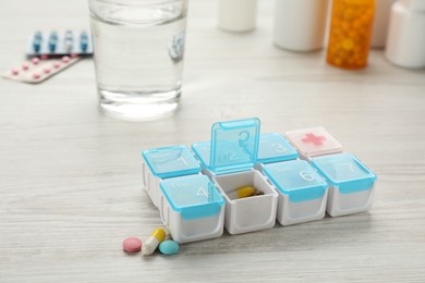 Plastic box with different pills on white wooden table