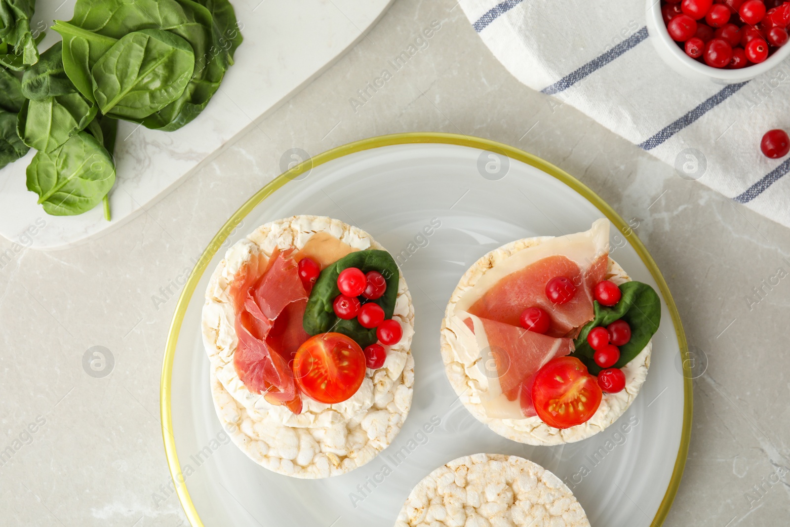 Photo of Puffed rice cakes with prosciutto, berries and basil on grey marble table, flat lay