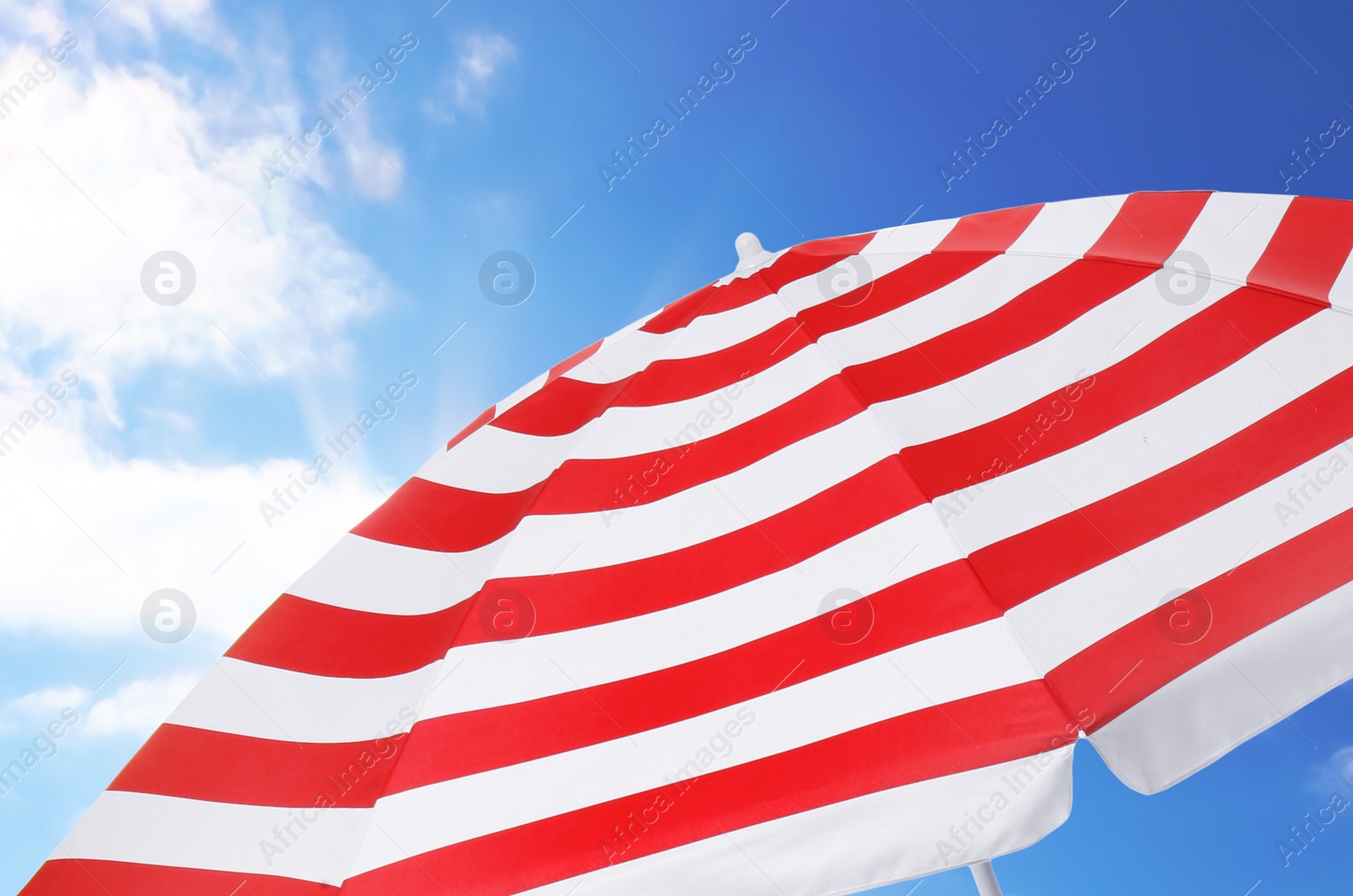 Image of Open big striped beach umbrella and beautiful blue sky with white clouds on background