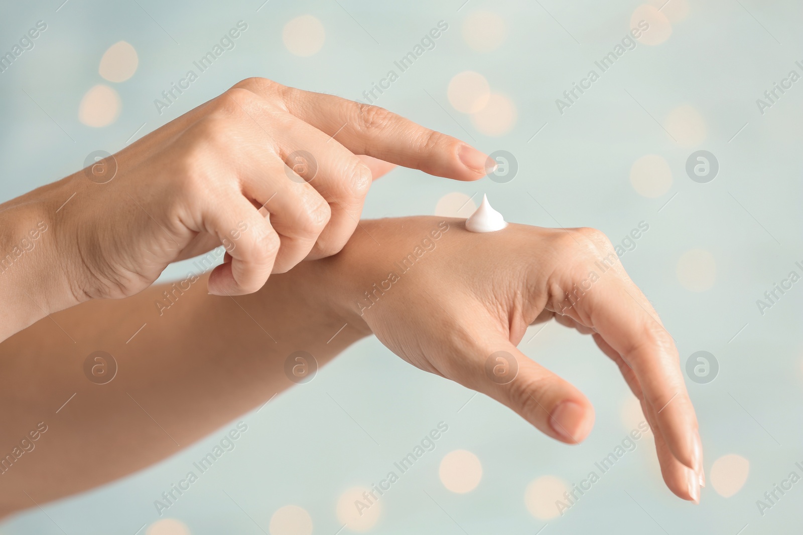 Photo of Woman applying hand cream on blurred background, closeup