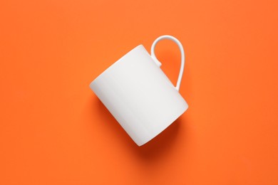 Photo of One white ceramic mug on orange background, top view