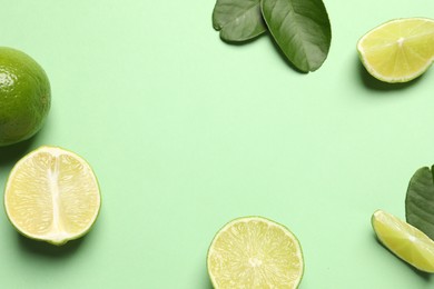 Whole and cut fresh ripe limes with leaves on light green background, flat lay