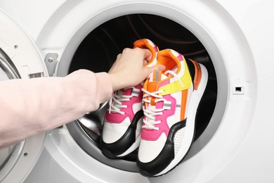 Woman putting stylish sneakers into washing machine, closeup