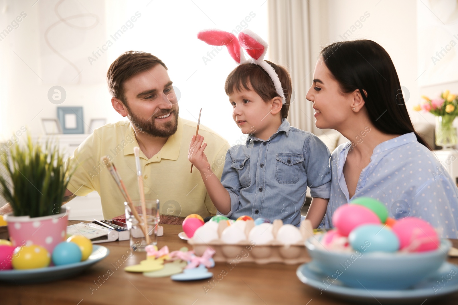 Photo of Happy family painting Easter eggs at table indoors