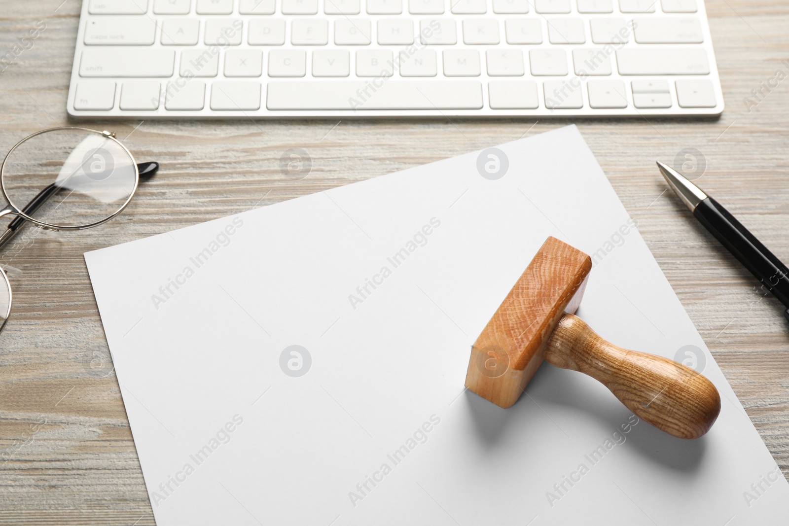 Photo of Blank sheet of paper, pen, glasses, keyboard and stamp on wooden table