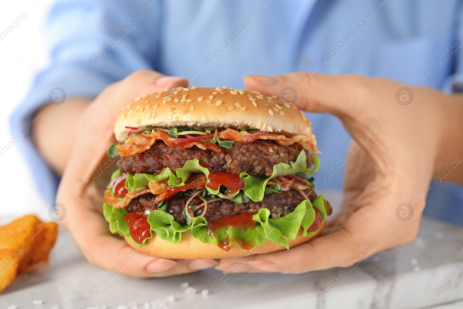 Photo of Woman holding tasty burger with bacon at table, closeup