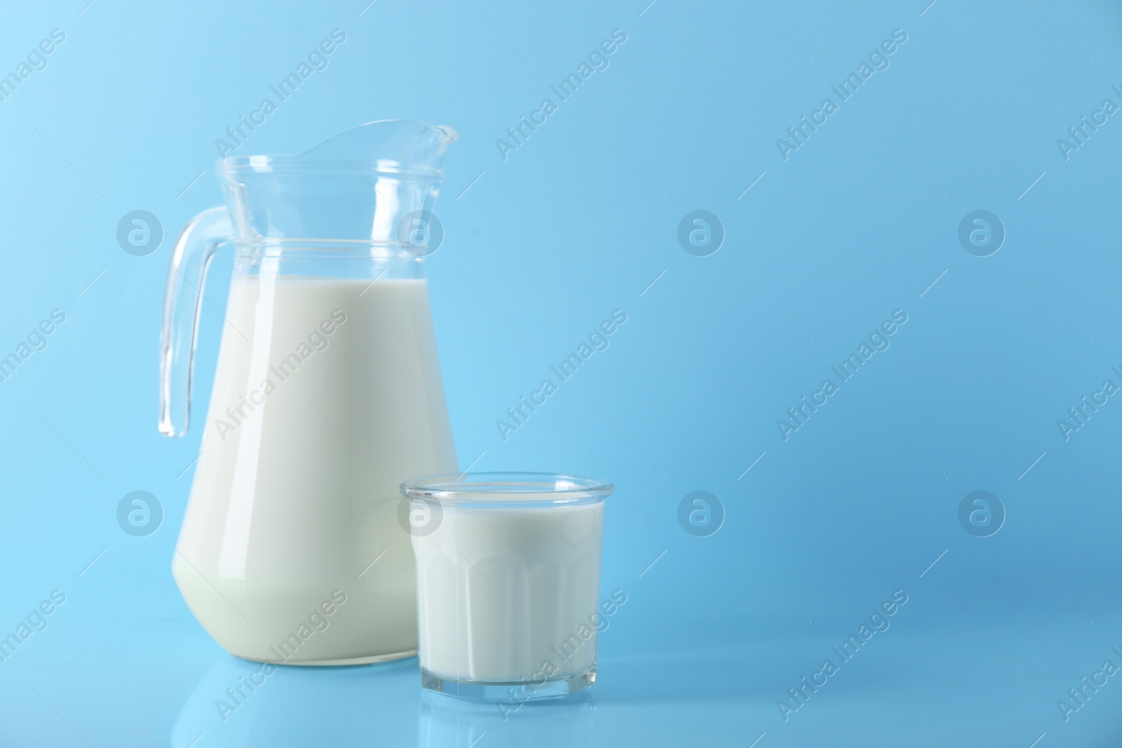 Photo of Jug and glass of fresh milk on light blue background, space for text