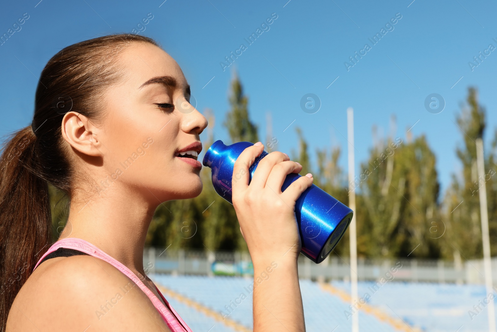 Photo of Sporty woman with bottle of water at stadium on sunny day. Space for text