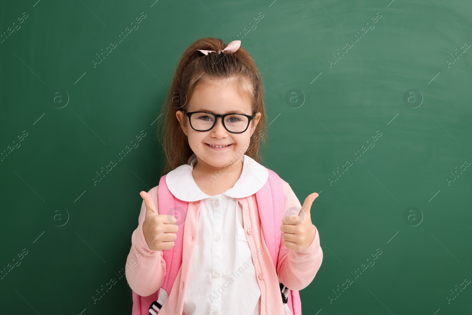 Photo of Happy little school child showing thumbs up near chalkboard