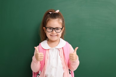 Photo of Happy little school child showing thumbs up near chalkboard