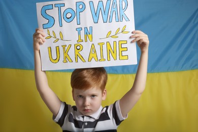 Boy holding poster Stop War in Ukraine against national flag