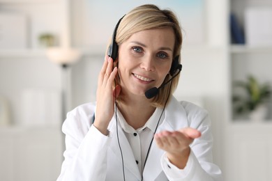 Photo of Portrait of smiling doctor in headphones having online consultation indoors