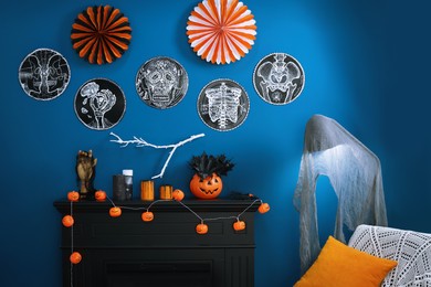 Photo of Jack-o'-lanterns and different Halloween decorations on black fireplace near blue wall