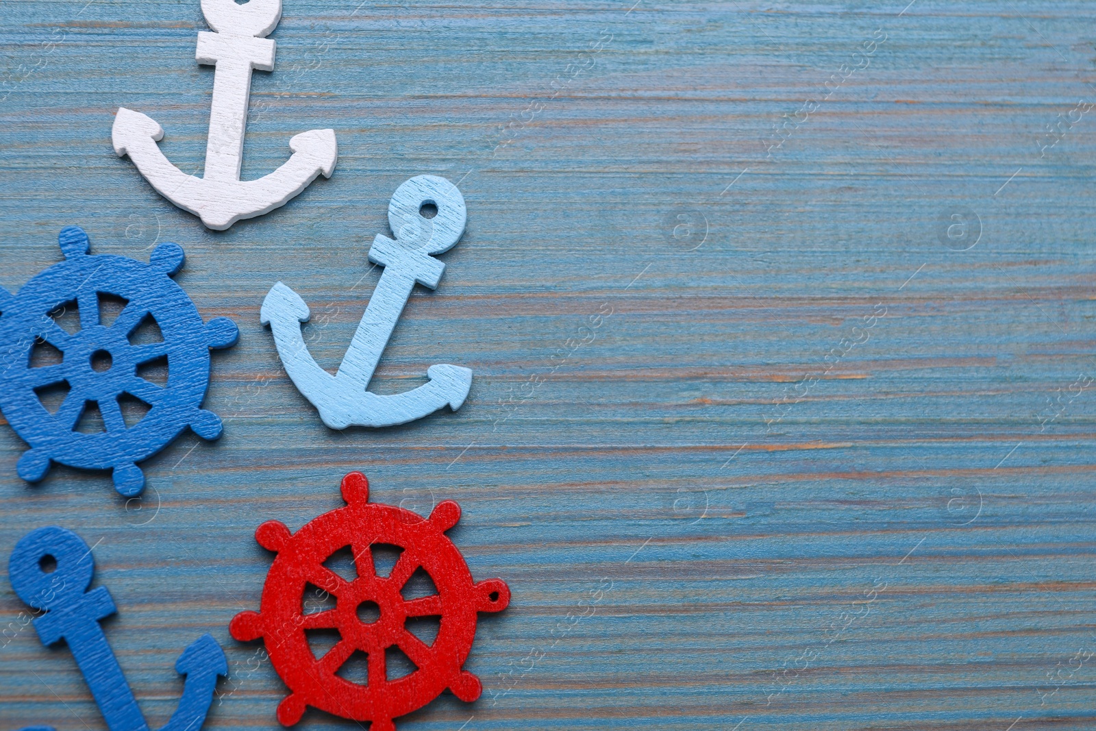 Photo of Anchor and ship wheel figures on light blue wooden table, flat lay. Space for text