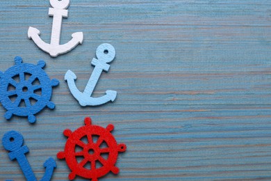 Photo of Anchor and ship wheel figures on light blue wooden table, flat lay. Space for text
