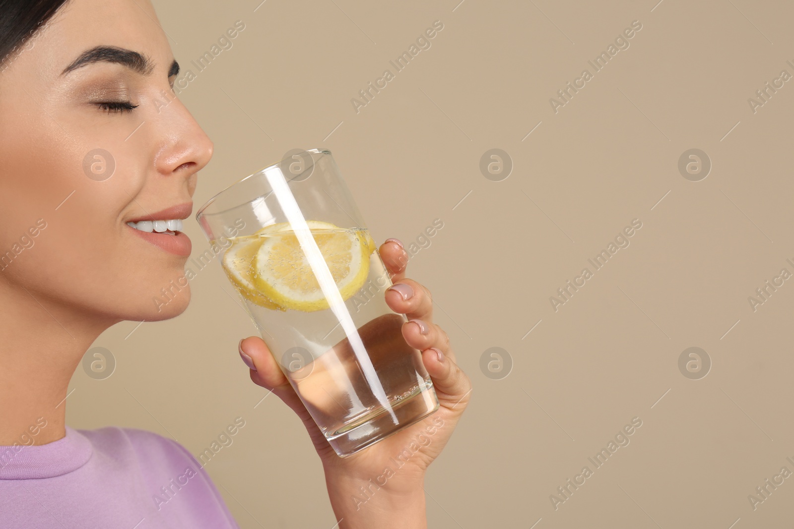 Photo of Beautiful young woman drinking tasty lemon water on beige background, closeup. Space for text