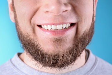 Young man with healthy teeth and beautiful smile on color background, closeup