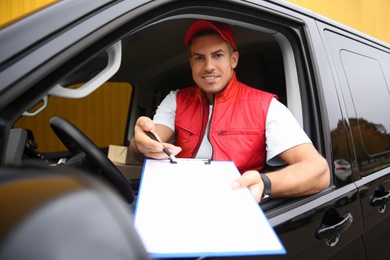 Photo of Courier giving clipboard with documents out of car window outdoors