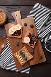 Different tasty toasts with nut butter and products on wooden table, flat lay