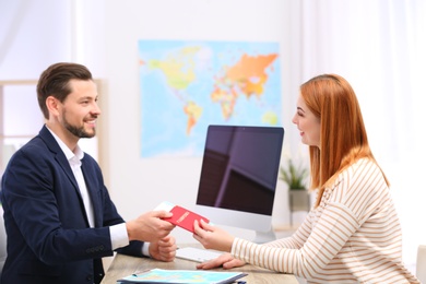 Photo of Male manager giving passport with ticket to client in travel agency