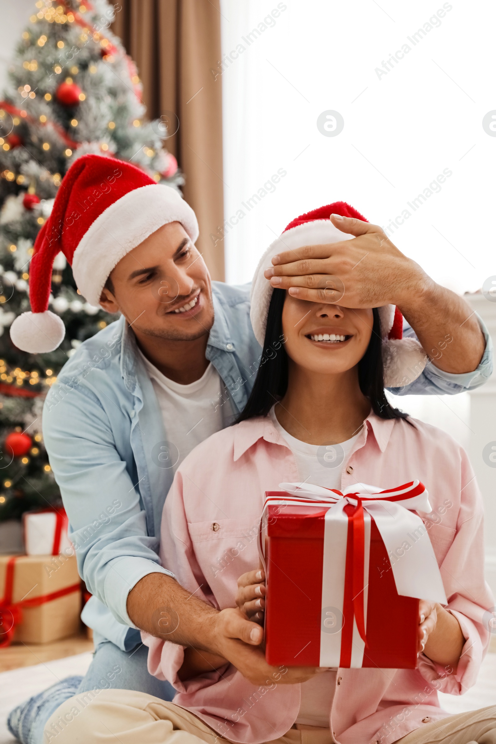 Photo of Happy couple in Santa hats with Christmas gift at home