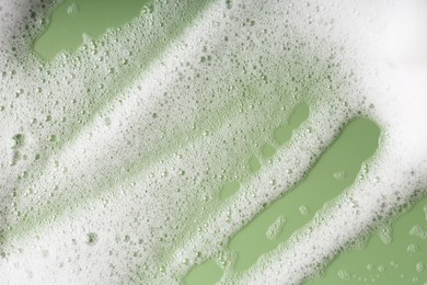 Photo of White fluffy foam on green background, top view