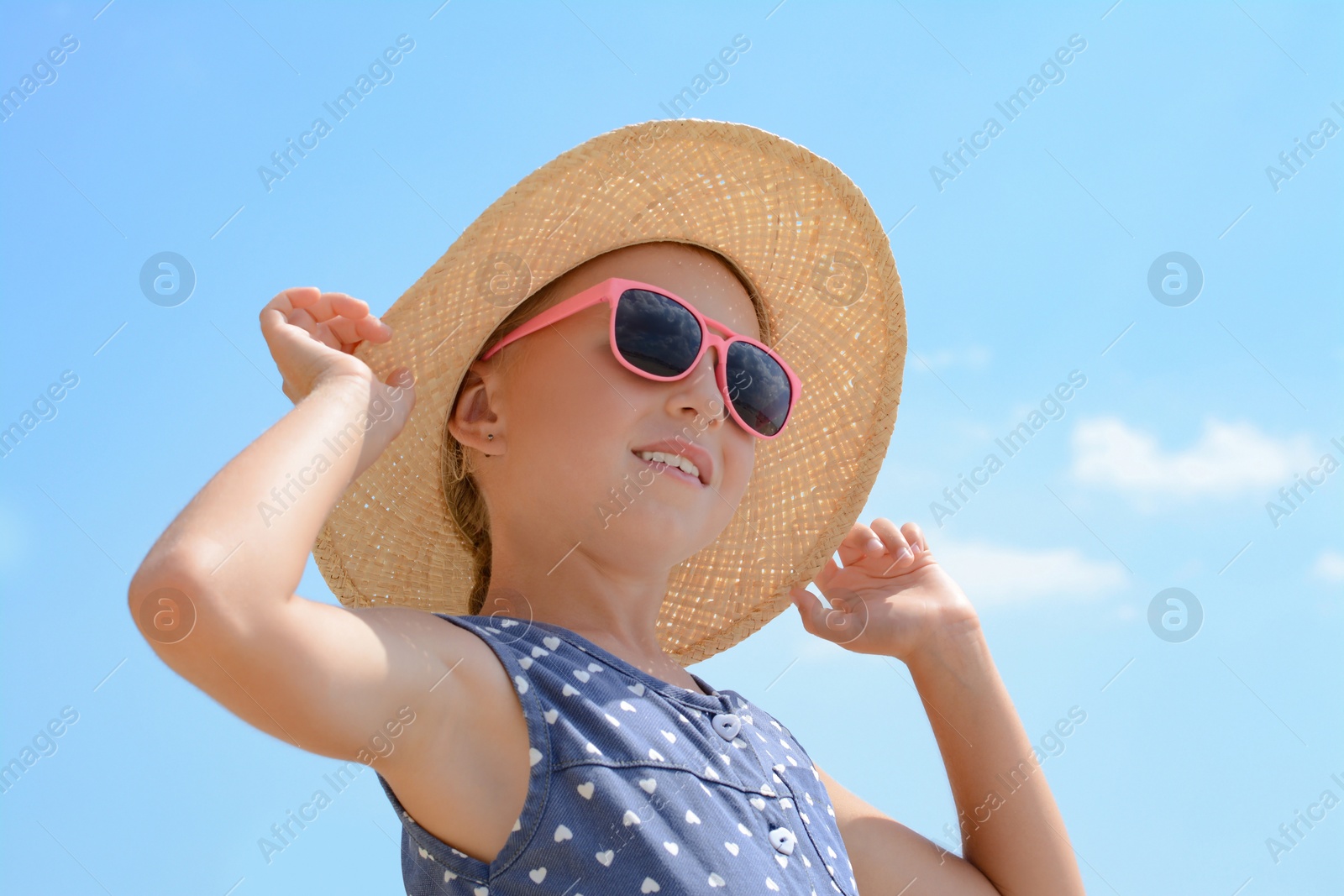 Photo of Little girl wearing sunglasses and hat at beach on sunny day