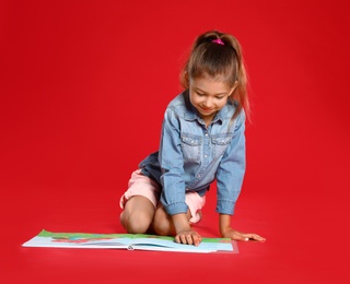 Cute little girl reading book on red background