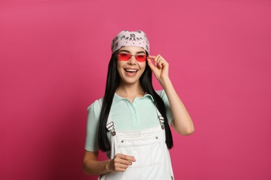 Young woman wearing stylish bandana and sunglasses on pink background