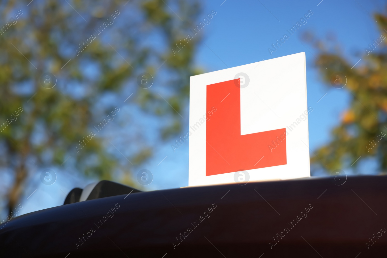 Photo of L-plate on car outdoors, low angle view with space for text. Driving school