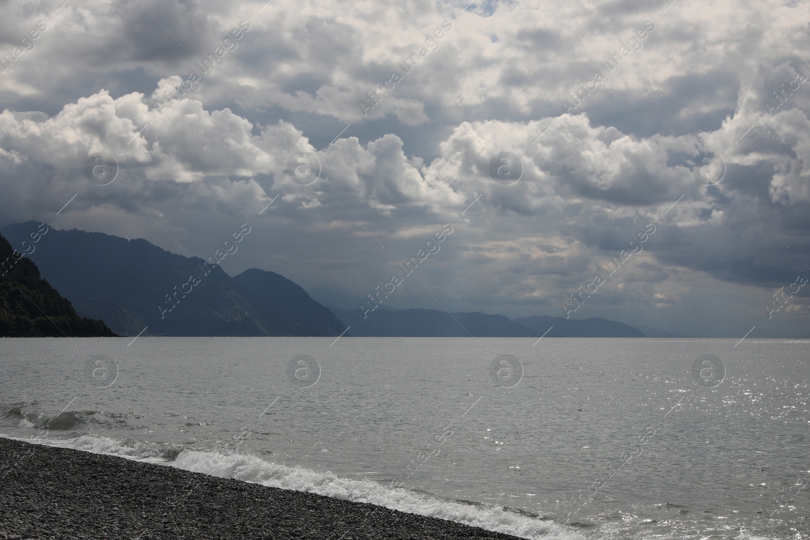 Photo of Picturesque view of beautiful sea shore and hills under gloomy sky with fluffy clouds