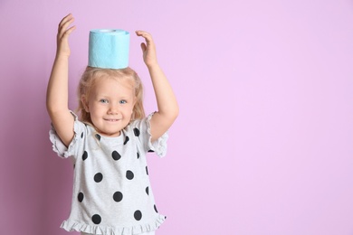 Cute little girl with toilet paper roll on color background. Space for text