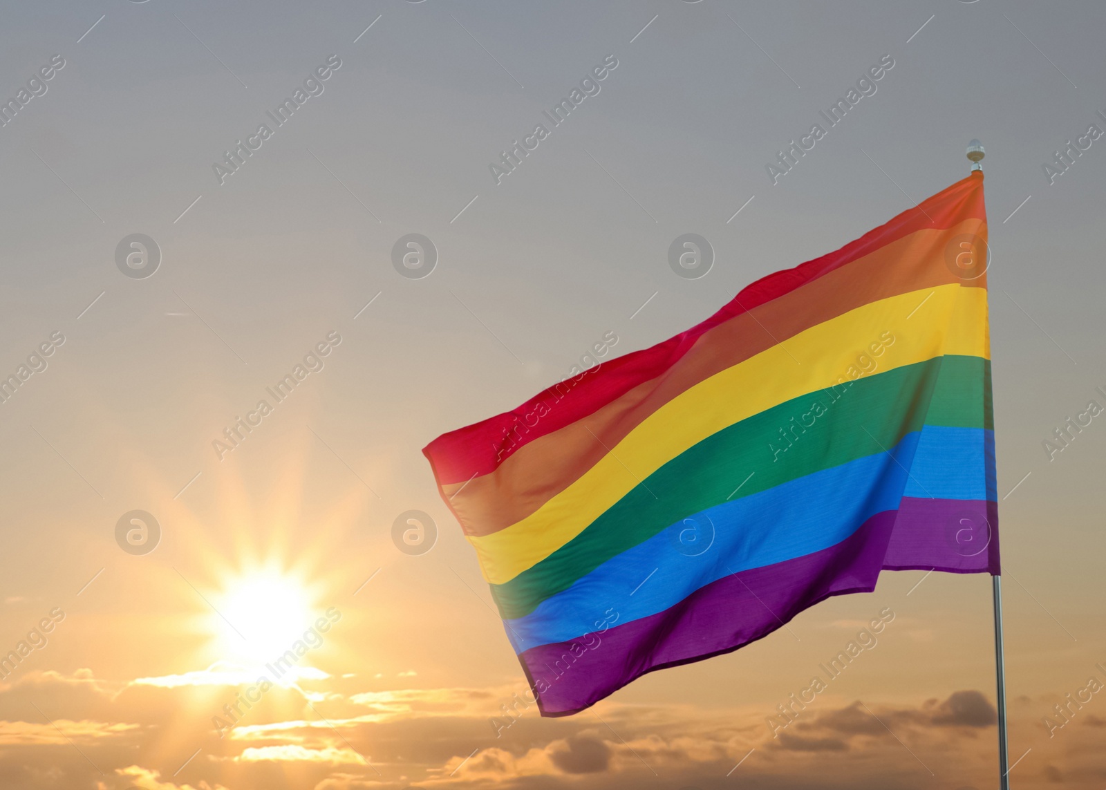 Image of Bright rainbow LGBT flag against sky at sunrise