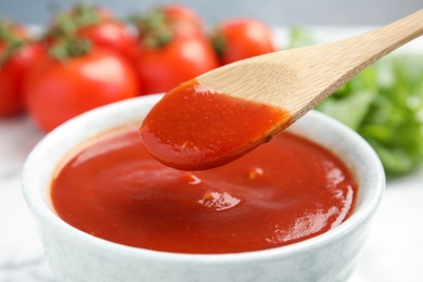Spoon with tomato sauce over bowl, closeup