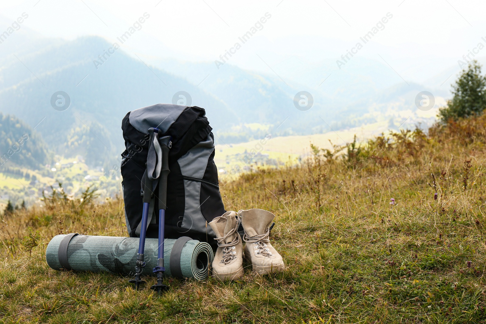 Photo of Backpack, trekking poles, boots and sleeping mat on hill, space for text. Tourism equipment