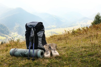 Photo of Backpack, trekking poles, boots and sleeping mat on hill, space for text. Tourism equipment