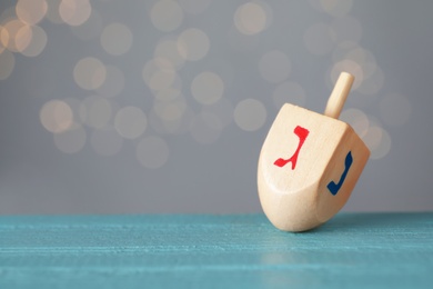 Photo of Hanukkah traditional dreidel with letters Gimel and Nun on wooden table against blurred lights. Space for text