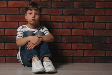 Photo of Little boy sitting on floor near brick wall, space for text. Children's bullying