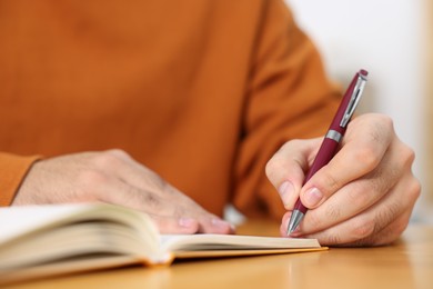 Young man writing in notebook at wooden table, closeup