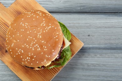 Photo of Tasty homemade cheeseburger with lettuce on grey wooden table, top view. Space for text