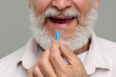 Senior man taking pill on grey background, closeup
