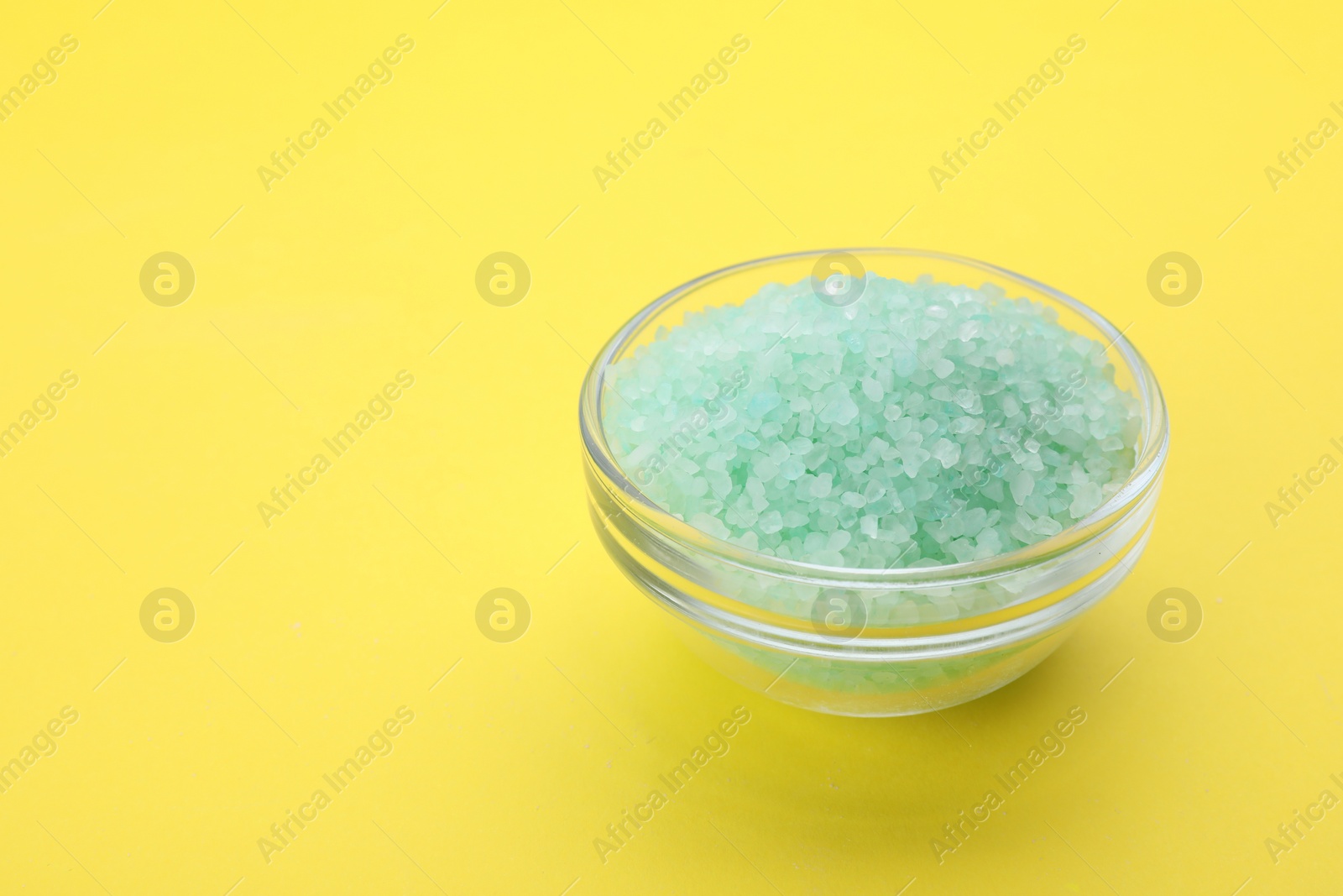 Photo of Bowl with turquoise sea salt on yellow background, space for text