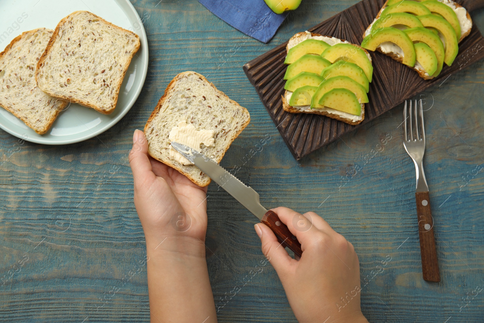 Photo of Woman making avocado sandwich at blue wooden table, top view