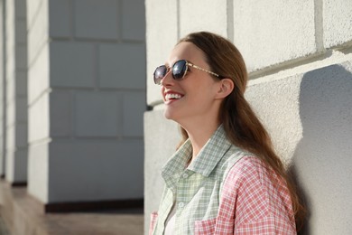 Smiling woman in sunglasses near building outdoors. Space for text
