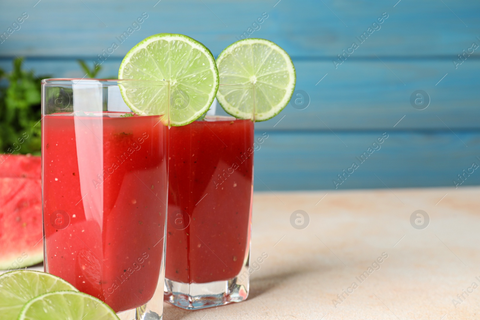 Photo of Tasty summer watermelon drink with lime in glasses on table against light blue background. Space for text