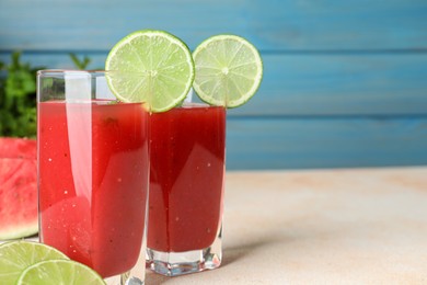 Photo of Tasty summer watermelon drink with lime in glasses on table against light blue background. Space for text