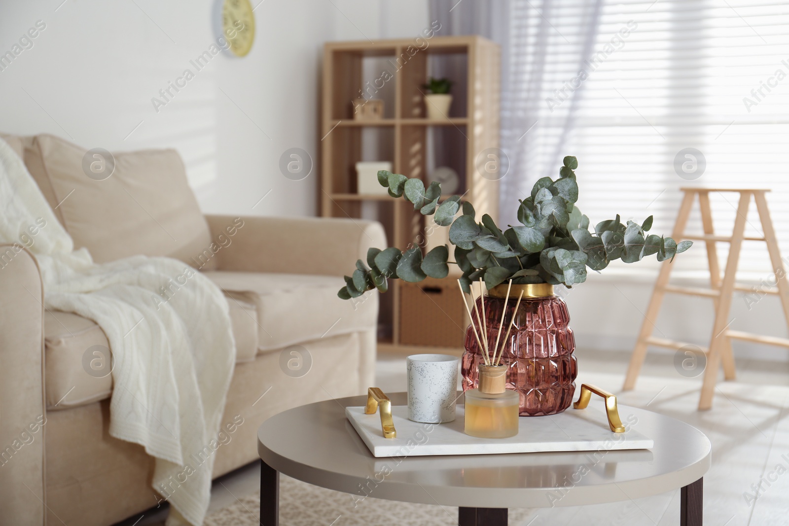 Photo of Bunch of eucalyptus branches and oil diffuser on table in living room. Interior design