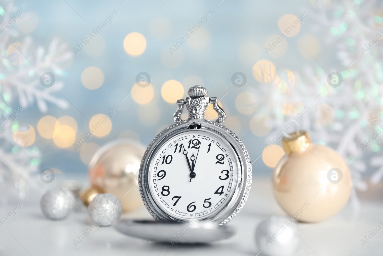 Photo of Pocket watch and festive decor on table against blurred lights. New Year countdown